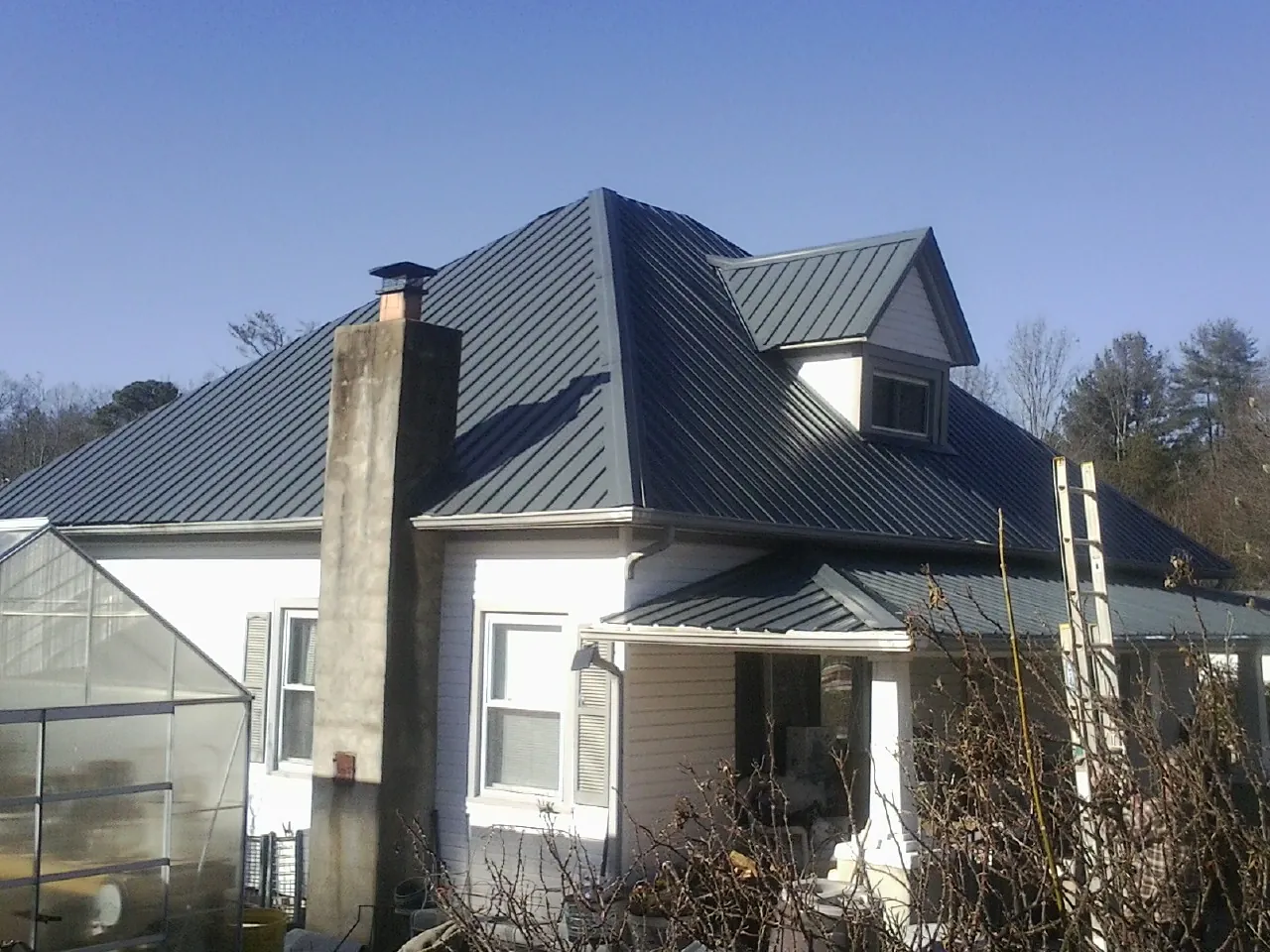 Dark blue standing seam metal roof on a white farmhouse with dormer — Slate & Tile Roof Repair by Roofing Brothers in La Motte