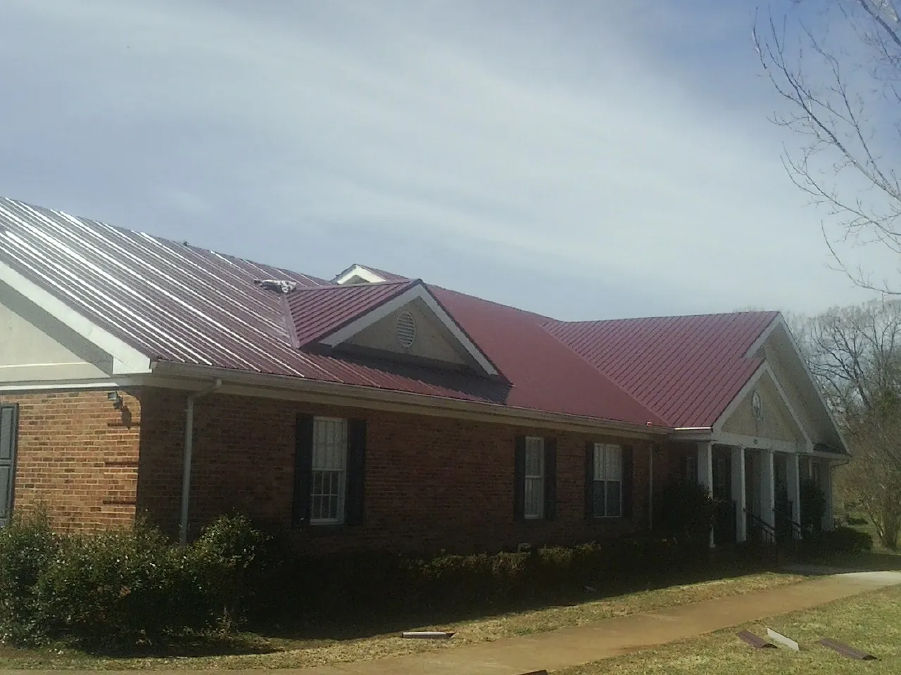 Red metal roof with gabled entries on a long brick building, from a Hail Damage Roof Repair job in La Motte
