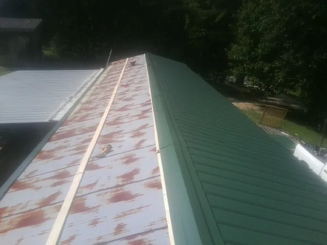 Old rusted panels beside newly installed green metal roofing — Wind Damage Roof Repair by Roofing Brothers in La Motte