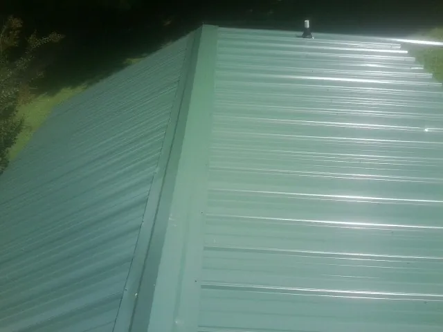 New green metal panels meeting at the ridge of a roof — Flat Roof Repair work by our crew in La Motte