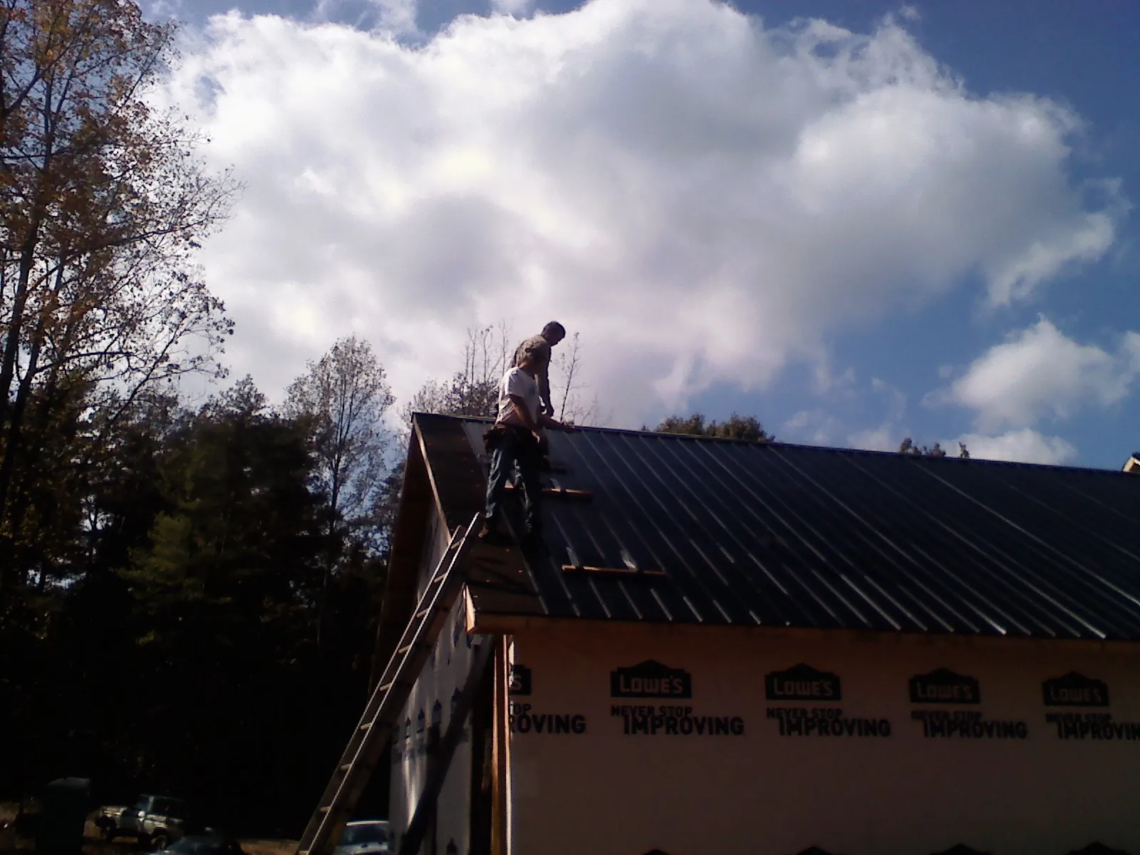 Roofer fastening dark metal panels high against a cloudy sky, from a Roof Inspection job in La Motte