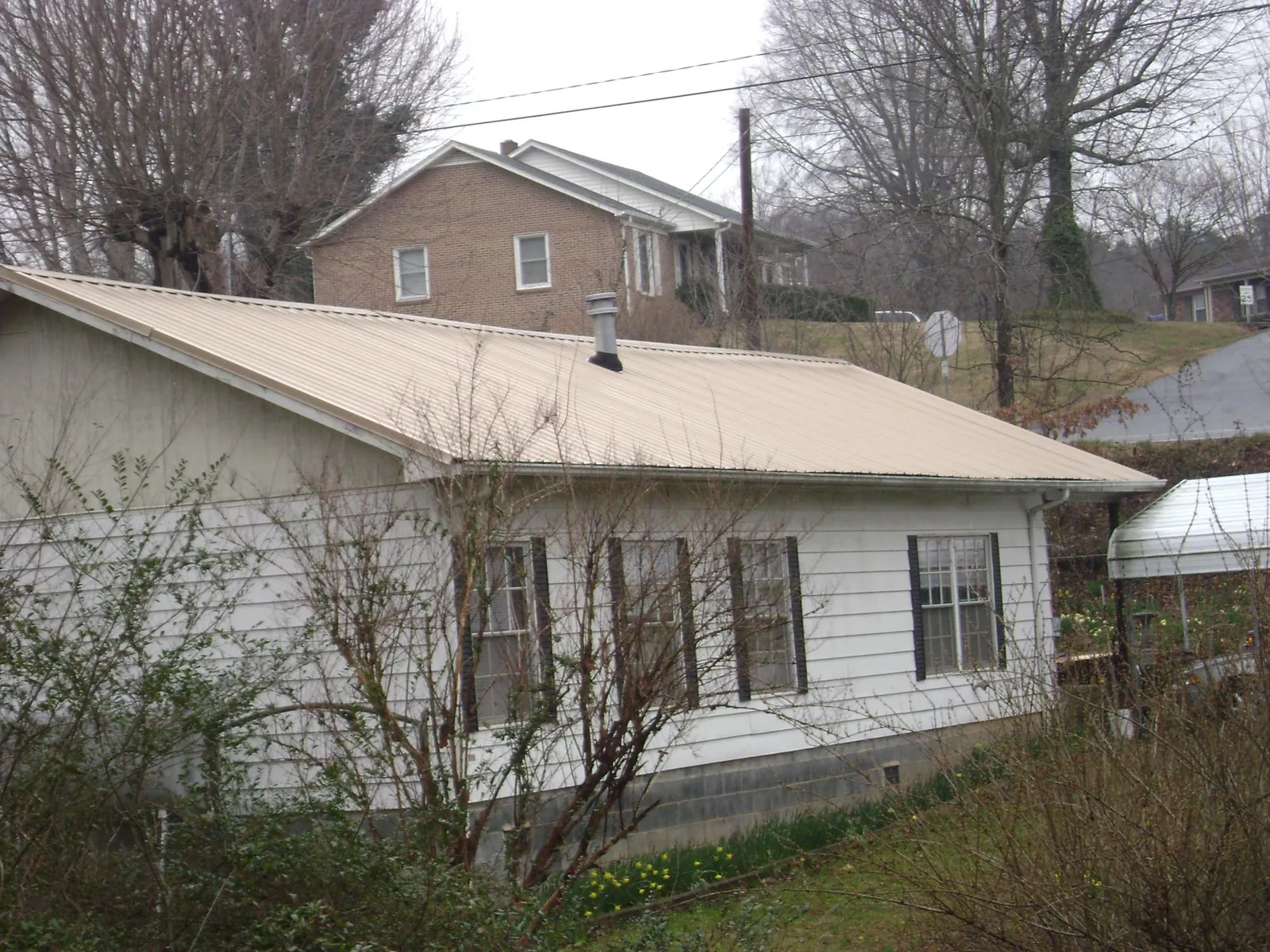 Tan metal roof on a white sided house set into a hillside — Commercial Roofing by Roofing Brothers in La Motte