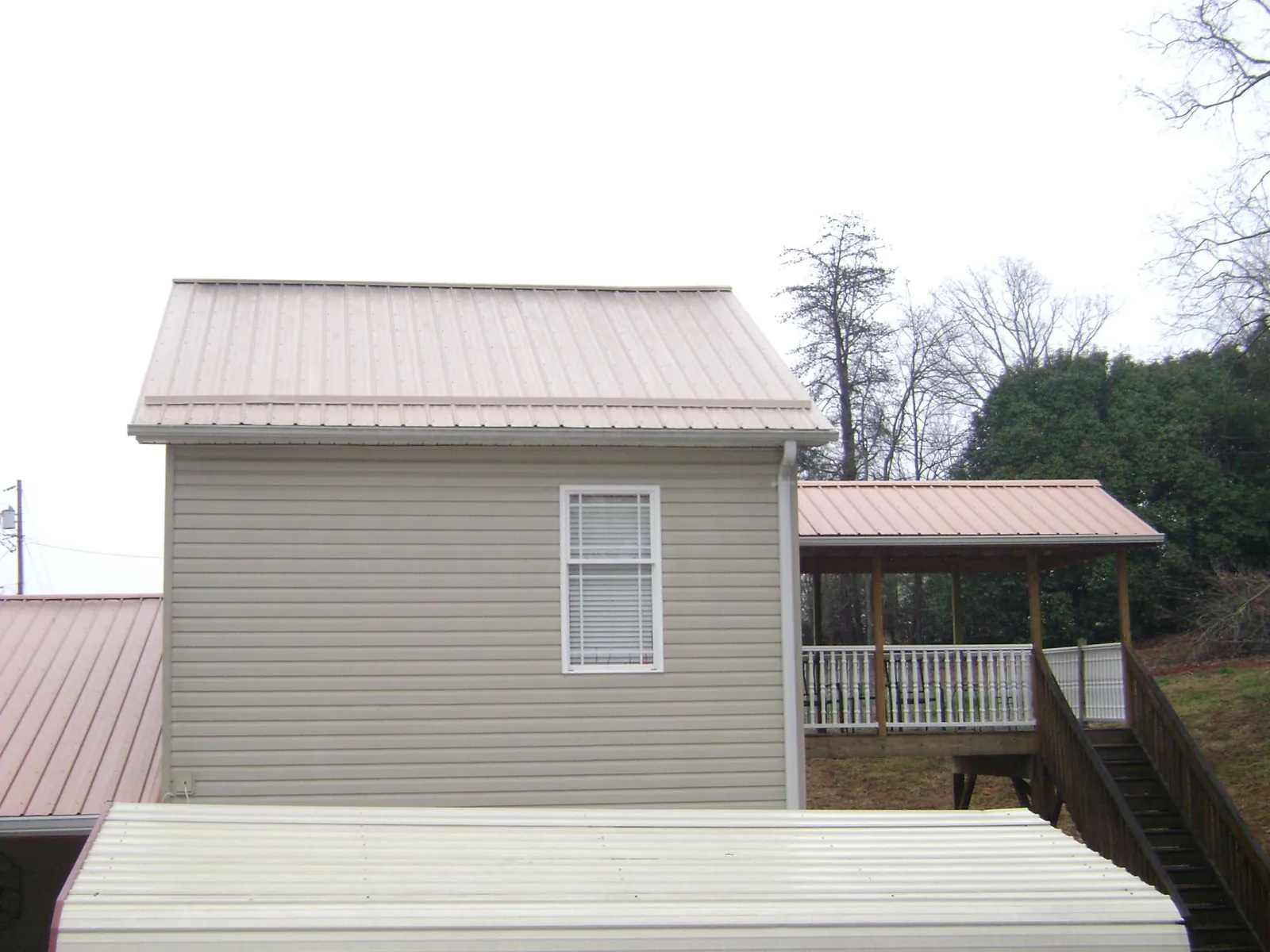 Tan metal roofs on a two story addition and attached porch, from a Roof Replacement job in La Motte